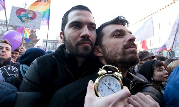Two men hugging at a street parade and holding a clock